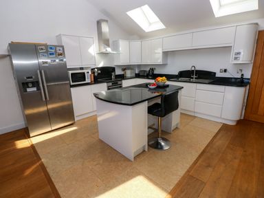 A kitchen with white cabinets black countertops a stainless steel refrigerator and a small island with a black chair at Gwelfor Marloes in Marloes Pembrokeshire