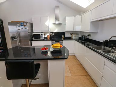 A kitchen with a black countertop island with a chair and fruit bowls next to white cabinets and stainless steel refrigerator at Gwelfor Marloes in Marloes Pembrokeshire