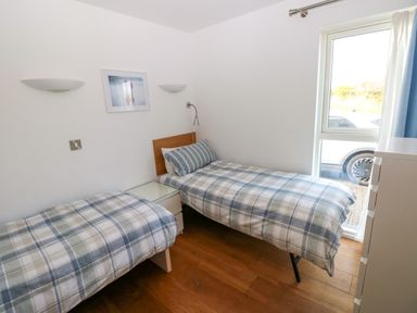 A small bedroom with two single beds a window bedside table and chest of drawers at Gwelfor Marloes in Marloes Pembrokeshire