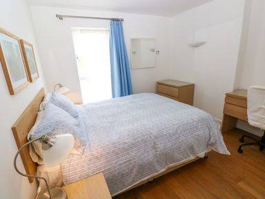 A bedroom with a double bed bedside lamp wooden furniture and a blue curtain at Gwelfor Marloes in Marloes Pembrokeshire