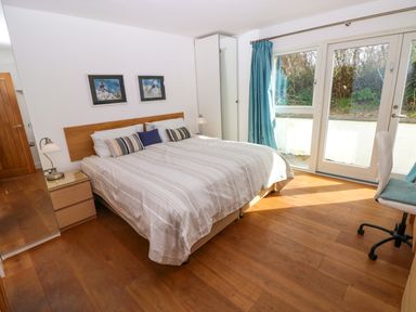 A bedroom with a double bed bedside tables lamps chair desk and glass doors with blue curtains at Gwelfor Marloes in Marloes Pembrokeshire