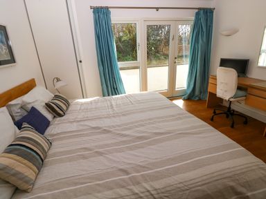 A bedroom with a bed pillows a desk with a chair and a computer and glass door with blue curtains at Gwelfor Marloes Marloes Pembrokeshire