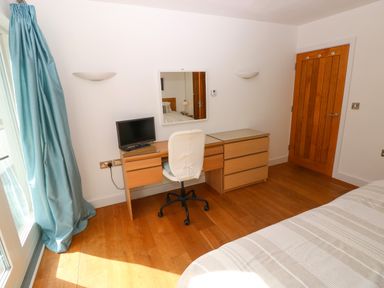 A bedroom corner with a wooden desk, white swivel chair, small TV, mirror, wooden door, and blue curtain at Gwelfor Marloes in Marloes Pembrokeshire