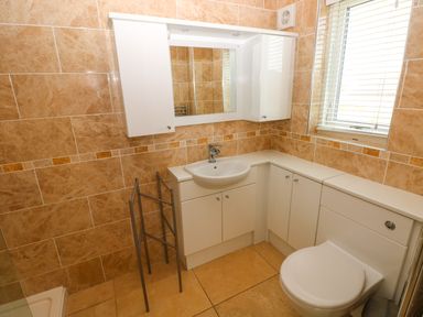 A bathroom with a corner sink, white cabinets, a toilet, a mirror cabinet, a metal towel rack, and beige tiled walls at Gwelfor Marloes in Marloes Pembrokeshire