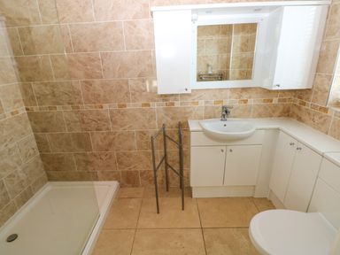 A bathroom with a shower area, white sink with cabinet, mirror, towel rack, and white toilet at Gwelfor, Marloes in Marloes Pembrokeshire