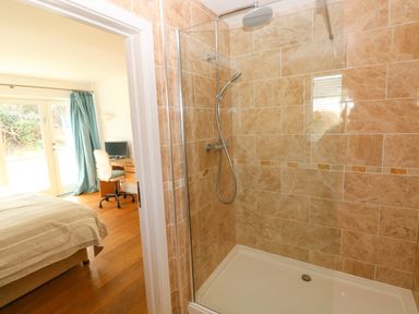 A tiled shower with a glass door and a rainfall showerhead next to a bedroom with a bed and a desk at Gwelfor Marloes in Marloes Pembrokeshire