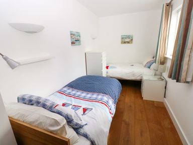 A small bedroom with two single beds, chest of drawers, nightstand, and window with curtains at Gwelfor, Marloes in Marloes Pembrokeshire
