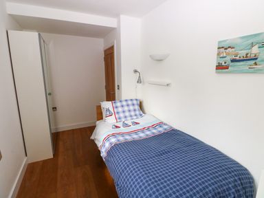 A small bedroom with a single bed with boat themed bedding a wall lamp a wardrobe and a painting of boats on the wall at Gwelfor Marloes in Marloes Pembrokeshire