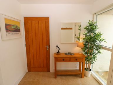 An entryway with a wooden door a wooden console table with a lamp plant and decorative items and a mirror on the wall at Gwelfor Marloes in Marloes Pembrokeshire