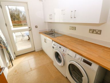 A utility room with a sink washing machine dryer white cabinets and wooden countertop at Gwelfor Marloes in Marloes Pembrokeshire