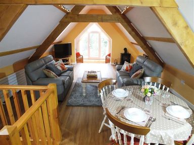 An attic living area with two sofas a coffee table a television a dining table set for four and exposed wooden beams at Pond Cottage in New Quay Ceredigion