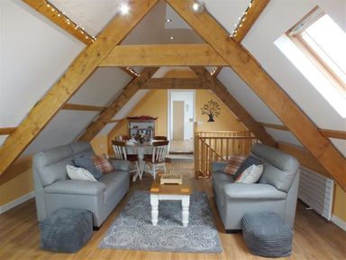 An attic living room with two grey sofas a wooden coffee table and a dining table with chairs at Pond Cottage in New Quay Ceredigion
