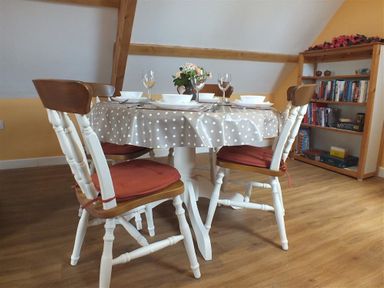 A dining room with a polka dot tablecloth on a round table set with dishes and glasses at Pond Cottage in New Quay Ceredigion