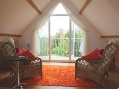 A room with two wicker chairs with cushions facing a glass door leading to a balcony at Pond Cottage in New Quay Ceredigion
