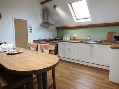 A kitchen with wooden table and chairs white cabinets countertop stove and skylight window at Pond Cottage in New Quay Ceredigion