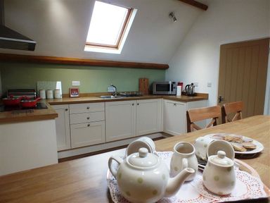 A kitchen with white cabinets wooden countertops a skylight a tea set on a table and wooden chairs at Pond Cottage in New Quay Ceredigion