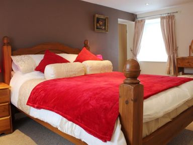 A bedroom with a wooden bed and red bedding with pillows at Pond Cottage in New Quay Ceredigion