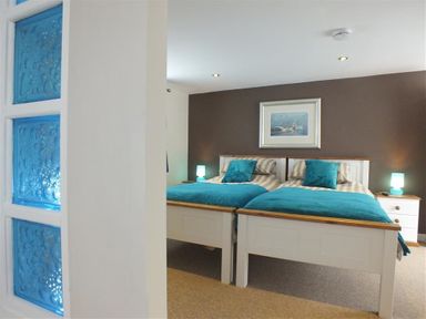 A bedroom with two beds with blue blankets and pillows two bedside tables with lamps and a framed picture on the wall at Pond Cottage in New Quay Ceredigion