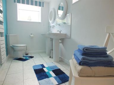 A bathroom with two sinks two mirrors a toilet blue patterned rugs and folded blue towels on a chair at Pond Cottage in New Quay Ceredigion