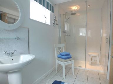 A bathroom with a pedestal sink a round mirror a chair with folded towels and a glass-enclosed shower at Pond Cottage in New Quay Ceredigion