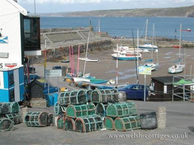 A harbor with stacked lobster pots and boats on the shore at Pond Cottage in New Quay Ceredigion