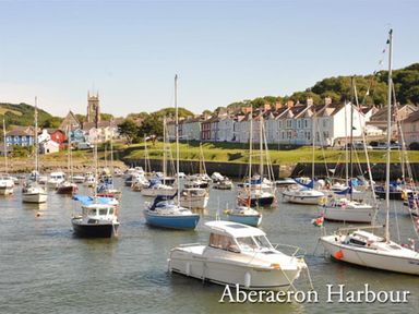 A harbour with boats and sailboats with houses and a church in the background at Aberaeron Harbour