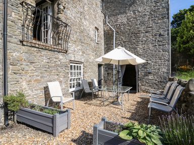 An outdoor patio with stone walls glass table white umbrella and chairs at Dewi Villa in Aberarth Ceredigion