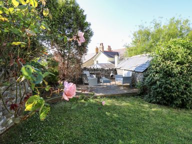 An outdoor patio area with grey wicker chairs and a table surrounded by stone walls and greenery at Dewi Villa in Aberarth Ceredigion