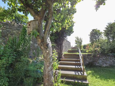 Wooden steps with handrail leading up a garden with trees and stone walls at Dewi Villa in Aberarth Ceredigion