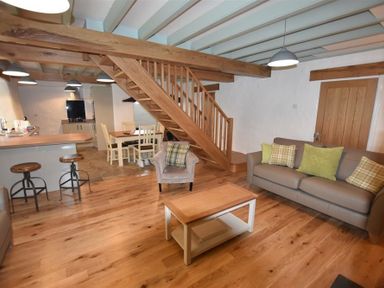 An open plan living area with wooden staircase gray sofa armchair coffee table and kitchen bar stools at The Old Farmhouse Kitchen in St Davids Pembrokeshire