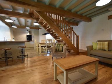 An open living area with wooden staircase wooden stools dining table chairs and a sofa with cushions at The Old Farmhouse Kitchen in St Davids Pembrokeshire