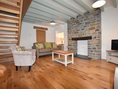 A living room with wooden floor sofa armchair coffee table and stone fireplace at The Old Farmhouse Kitchen in St Davids Pembrokeshire