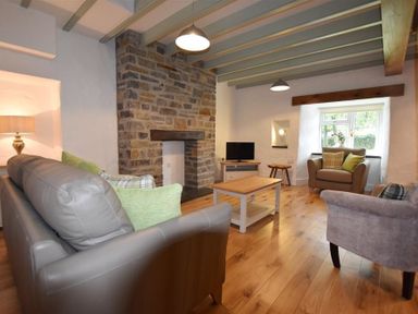A living room with gray sofa armchairs wooden coffee table stone fireplace and window at The Old Farmhouse Kitchen in St Davids Pembrokeshire
