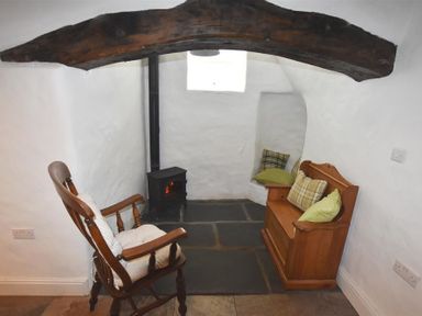 A small sitting area with a wooden rocking chair a wood stove and a wooden bench with cushions at The Old Farmhouse Kitchen in St Davids Pembrokeshire