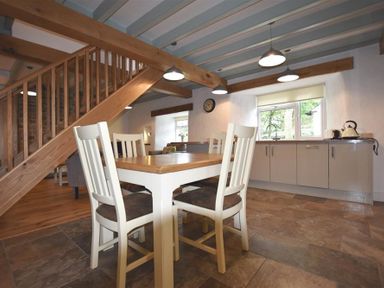 A kitchen and dining area with a wooden table and four chairs under wooden stairs at The Old Farmhouse Kitchen in St Davids Pembrokeshire
