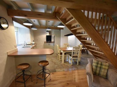A kitchen and dining area with wooden stools a table and chairs and a wooden staircase at The Old Farmhouse Kitchen in St Davids Pembrokeshire