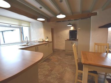 A kitchen with wooden countertops, beige cabinets, a dining table with chairs, and pendant lights at The Old Farmhouse Kitchen in St Davids Pembrokeshire