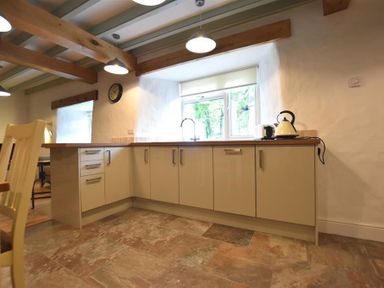 A kitchen with beige cabinets wooden countertop a kettle toaster under window with wooden beams on ceiling at The Old Farmhouse Kitchen in St Davids Pembrokeshire