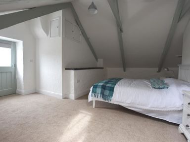 A bedroom with a single bed with white bedding and teal throw at The Old Farmhouse Kitchen in St Davids Pembrokeshire