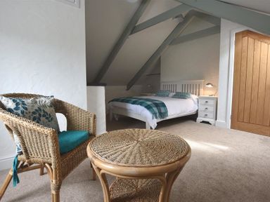 A bedroom with a bed a wooden door a wicker chair and table at The Old Farmhouse Kitchen in St Davids Pembrokeshire