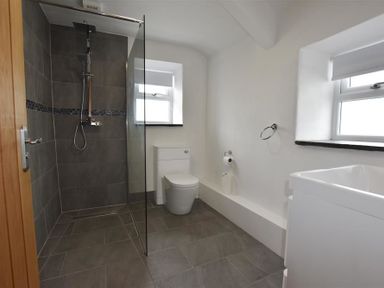 A bathroom with a walk-in shower a toilet and a sink under two windows at The Old Farmhouse Kitchen in St Davids Pembrokeshire