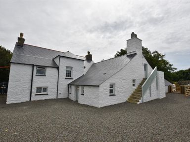 The exterior of a white stone house with multiple chimneys and a stone staircase leading to an upper door at The Old Farmhouse Kitchen in St Davids Pembrokeshire