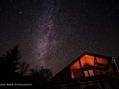 A night sky filled with stars above a lit balcony of a wooden house at Dan Castell Cottage in Llandeilo Carmarthenshire