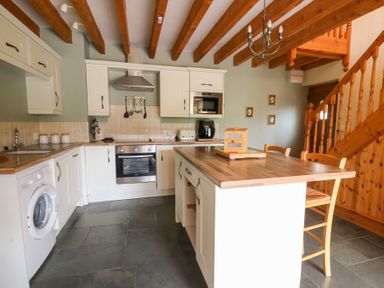 A kitchen with appliances and a staircase at Dan Castell Cottage in Llandeilo, Carmarthenshire