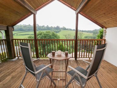 A balcony with chairs and a table overlooking hills at Dan Castell Cottage in Llandeilo, Carmarthenshire