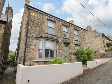 A stone exterior house with three windows and a green door with white fences at Nevern House in Newport Pembrokeshire