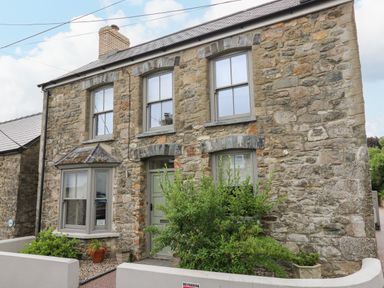 Stone exterior of a two story house with three windows a green door and plants by the entrance at Nevern House in Newport Pembrokeshire