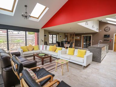 An open living room and kitchen area with white sofas yellow cushions glass coffee table dining table and chairs at Nevern House in Newport Pembrokeshire