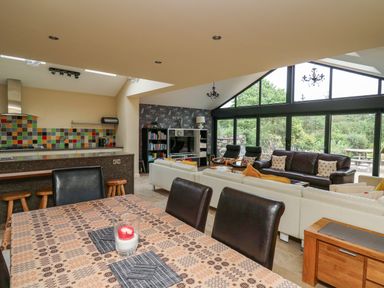 An open plan living area with a dining table a kitchen with multicolored tiled backsplash and a seating area with sofas and large windows at Nevern House in Newport Pembrokeshire