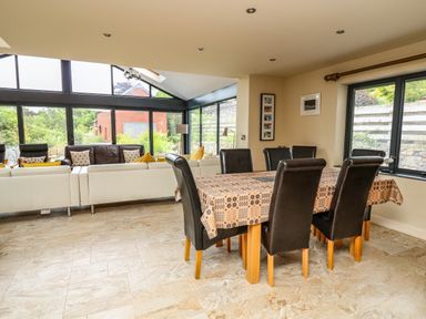 A dining area with a table and six chairs next to a seating area with sofas and large windows at Nevern House in Newport Pembrokeshire